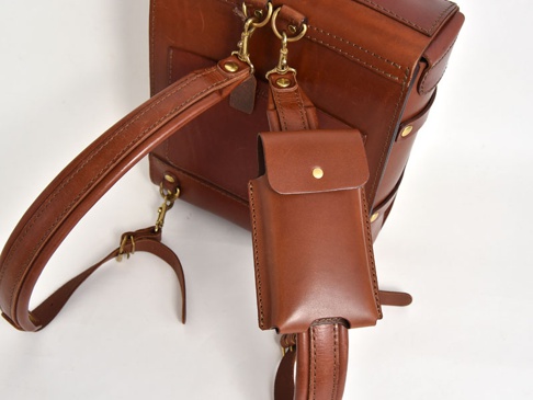 職人手作皮革三用手機收納包 (KM-1) M，採用棕色皮革製成，配有金屬釦環和可拆卸揹帶。收納包設計簡潔，可用於收納手機或其他小物。