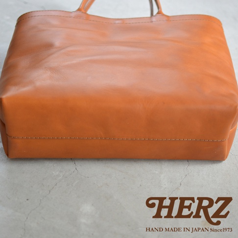 HERZ 職人手作皮革托特包，顏色為棕褐色，材質為皮革，包款為肩背款式，底部有縫線細節。