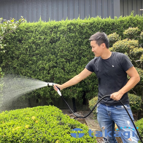 男性手持白色與黑色組合的水槍，對著綠色植物噴水，水流呈扇形散開。