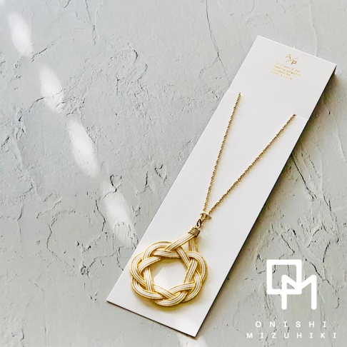 金色細鍊搭配白色與金色的日本水引花結，組成一個圓形墜飾，懸掛在鍊子上。