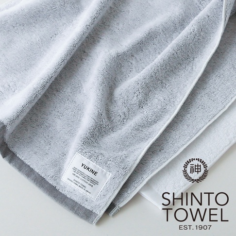 兩條蓬厚毛巾，一條為淺灰色，另一條為白色，皆為有機棉材質，帶有品牌標籤。