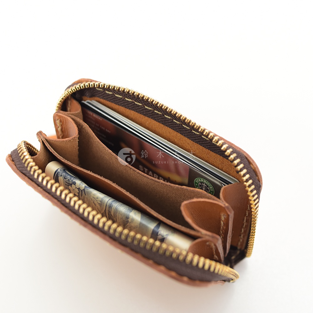 職人手作的棕色皮革收納錢包，拉鍊設計，內部可見多個隔層，裝有信用卡和一支筆。