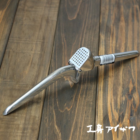 銀色不鏽鋼壓蒜器，帶有圓孔的壓蒜槽和一個長柄，置於深色木紋背景上。