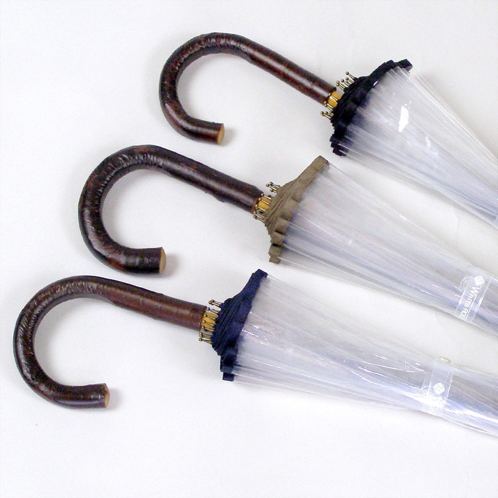 三把職人高級樺木透明傘，傘柄為彎曲的深棕色樺木材質，傘面由透明塑膠製成，傘頭有深藍色和卡其色兩種布質裝飾，傘骨結構可見。