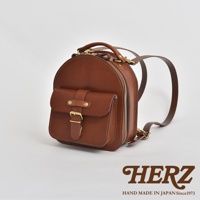 職人手作咖啡色皮革迷你後背包，圓潤造型，正面有翻蓋口袋與金屬扣環，側邊有拉鍊，附有皮革揹帶。