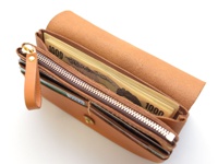職人手作皮革旅行用長夾，淺棕色皮革材質，內含多疊日圓鈔票與信用卡，拉鍊及金屬扣環為銀色。