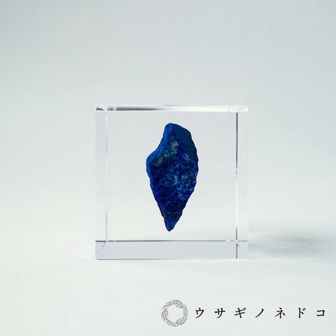 透明立方體內嵌一塊深藍色、帶有金屬光澤的青金石原石，青金石表面有粗糙紋理和少量雜質。