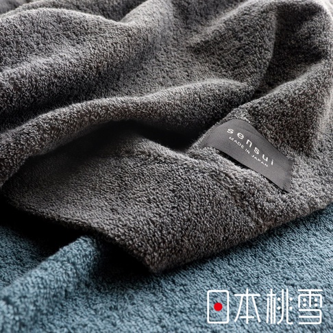 一條深灰色雙面毛圈毛巾，標有「sensui MADE IN JAPAN」字樣，疊在下方一條藍綠色毛巾上，展現細緻的織紋。