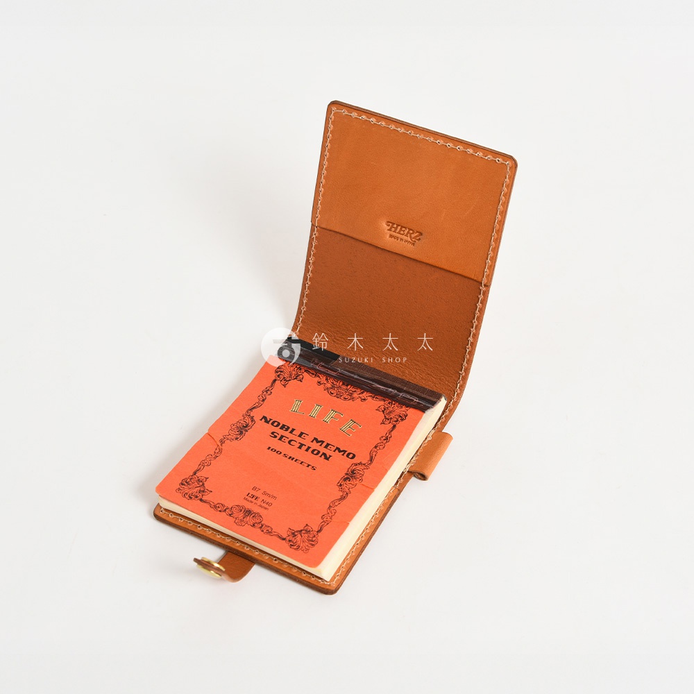 職人手作皮革便利貼收納套，淺棕色皮革製成，可收納橘色封面的「LIFE NOBLE MEMO SECTION」便利貼。收納套內側有品牌標誌，整體設計簡潔實用。
