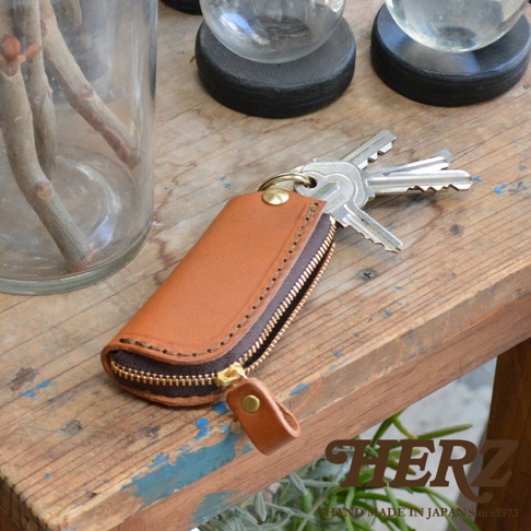 職人手作皮革鑰匙包，咖啡色皮革，附有黃銅拉鍊和掛環，可收納多把鑰匙，展現簡約實用的設計風格。