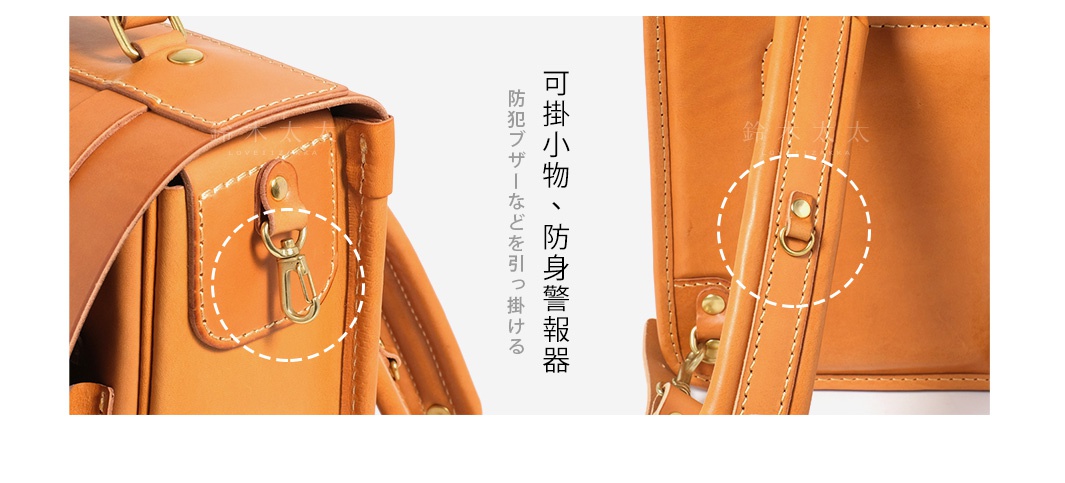 職人手作皮革小學生書包，展示側邊皮質掛鉤與肩帶D型環的細節，皮革呈現自然的棕褐色。
