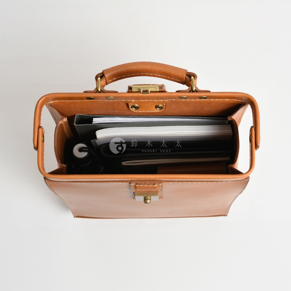 頂部視角展示一個棕褐色皮革製的杜勒斯商務後背包，包內裝有筆記本、文件夾及黑色物品。包身採用縫線工藝，配有金屬鎖扣及提把。