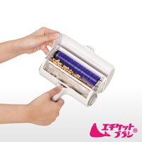 雙層除塵滾輪，白色外殼，內含紫色毛刷滾輪及收集髒污的隔層，裝有貓砂顆粒和棉絮。