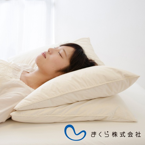 兩張米白色羽絨枕疊放，一位女性仰躺其中，頭部倚靠在枕頭上，面部閉眼。枕頭材質柔軟，表面有細膩的壓紋。