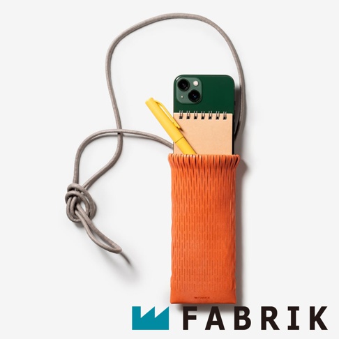 FABRIK 橘色皮革隨形貼合伸縮小包，內含綠色手機、米色筆記本和黃色筆，並以灰色繩子掛在項鍊上。