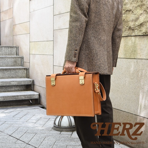 職人手作皮革兩用機師箱 BC-31-H，淺棕色皮革，配有金色金屬扣環和提把，可肩背或手提。