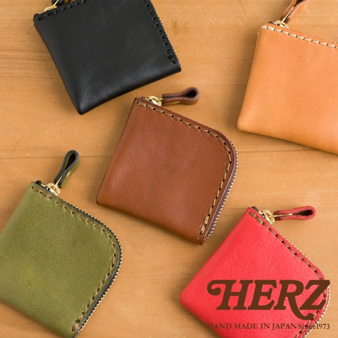 木質桌面上擺放著五個日本HERZ職人手作皮革零錢包，分別呈現黑、米色、棕色、橄欖綠與紅色，每個包款皆採精緻車縫線搭配拉鍊設計，展現簡約實用的皮革工藝質感。