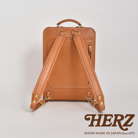 職人手作皮革商務電腦後背包 R-25，經典棕色，採用真皮材質，設計簡約，配有可調節的皮革肩帶、拉鍊隔層及品牌標誌。