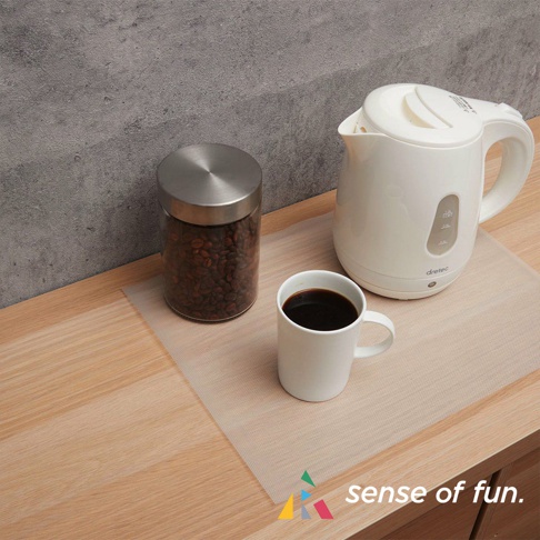 淺色半透明捲筒式砧板保潔墊片，置於木質檯面上，上面放有裝滿咖啡豆的玻璃罐、白色馬克杯及白色電熱水壺。