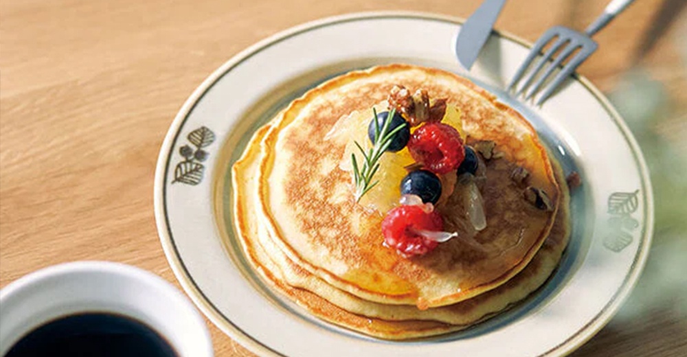 Anyware 美濃燒葉紋復古溫潤甜點盤，盤身為米白色，邊緣飾有線條勾勒的葉子圖案。盤中盛放著疊起的鬆餅，淋有糖漿，並點綴著覆盆子、藍莓、核桃碎和迷迭香。