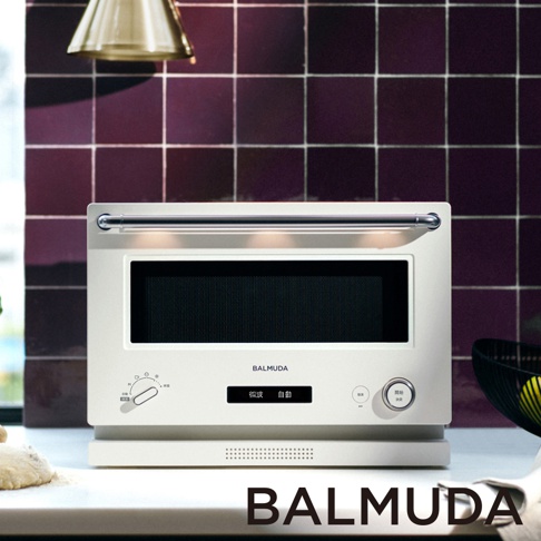 The Range 20L微波烤箱，米白色機身，配有銀色金屬把手。正面有黑色玻璃門、顯示螢幕及操作旋鈕和按鈕。背景是深紫色方形磁磚牆。