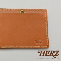 淺棕色皮革橫式證件夾，採用手工縫線，正面右下角有「HERZ」品牌壓紋，上方有金屬掛環。