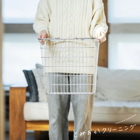一個大型不鏽鋼網狀收納籃，由銀色金屬製成，有提把，由一個人拿著。