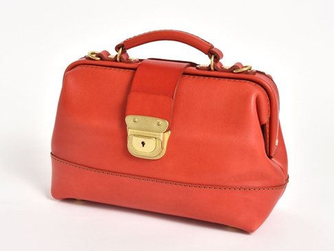 紅色皮革製成的手提包，帶有金色鎖扣和提把，可作為單肩包使用。