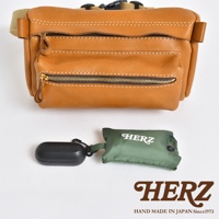 職人手作皮革兩用腰掛斜背包，採用棕褐色皮革製成，配有黃銅色拉鍊和米色織帶。包款具有多個拉鍊隔層，並展示了黑色耳機盒和綠色收納袋。