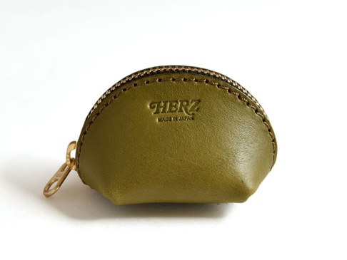 橄欖綠皮革貝殼造型零錢包，配有黃銅拉鍊及手工縫線，正面壓印有「HERZ」及「MADE IN JAPAN」字樣。