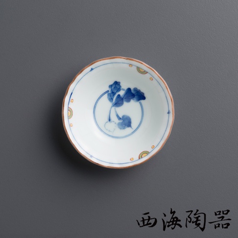 白色陶瓷小菜碟，內側繪有藍色蘿蔔圖案，外緣飾有黃色與綠色扇形裝飾，碟邊呈現波浪狀，邊緣帶有土黃色。