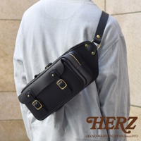 黑色皮革騎士斜背包，採用職人手作工藝，配有黃銅釦環、拉鍊和铆釘，展現復古風格。