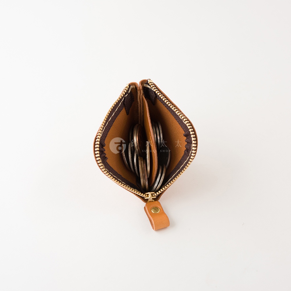 一個採用棕色皮革製作的日本HERZ職人手作分隔零錢包，採拉鍊開口設計並以俯視角度呈現，內部中間設有皮革隔層，裝有少量硬幣，包身下方掛有一個帶有金色鉚釘的皮革拉繩。