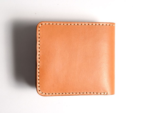 淺棕色皮革製成的雙折短夾，外觀簡潔，邊緣有手工縫線，整體呈現自然皮革質感。