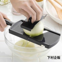 一只手正握著黑色塑膠刨絲器，將一顆洋蔥推過刀片，切成薄片落入玻璃碗中，碗底已有部分切好的洋蔥絲。