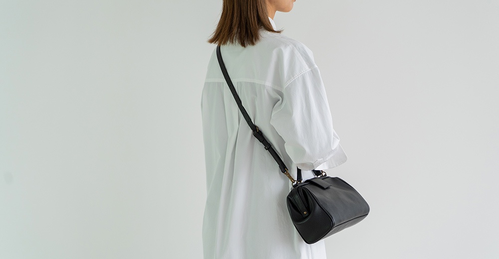 穿著白色襯衫的人側身背著一個黑色皮革手提包