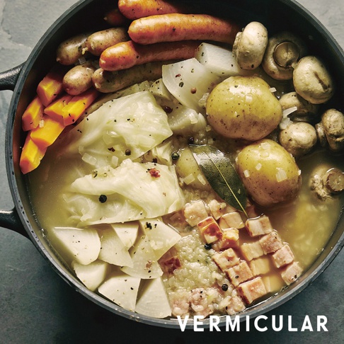 一個裝有香腸、高麗菜、馬鈴薯、胡蘿蔔、蘑菇和肉丁的陶鍋，鍋內湯汁看起來很美味。