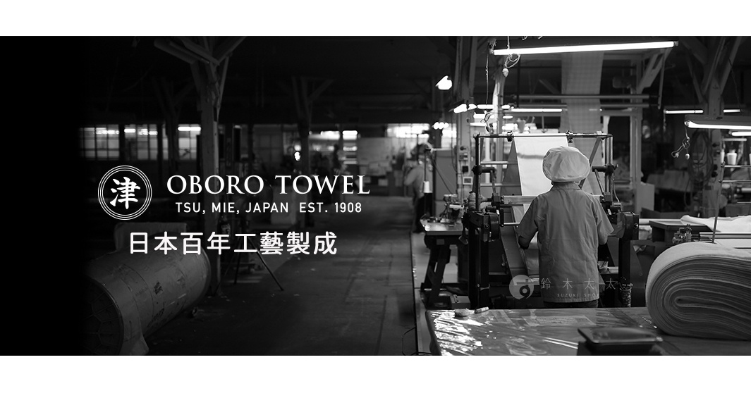 黑白影像，展示日本傳統毛巾工廠內部。一位工人頭戴帽子，專注操作機器，前方機器正在生產布料。左側印有「津」字標誌、OBORO TOWEL字樣及「日本百年工藝製成」的日文說明。