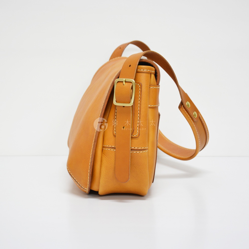 職人手作皮革復古翻蓋郵差包，採用天然皮革材質，呈現溫潤的焦糖棕色。包款帶有經典翻蓋設計，搭配金屬扣環與車縫線細節，風格簡約實用。