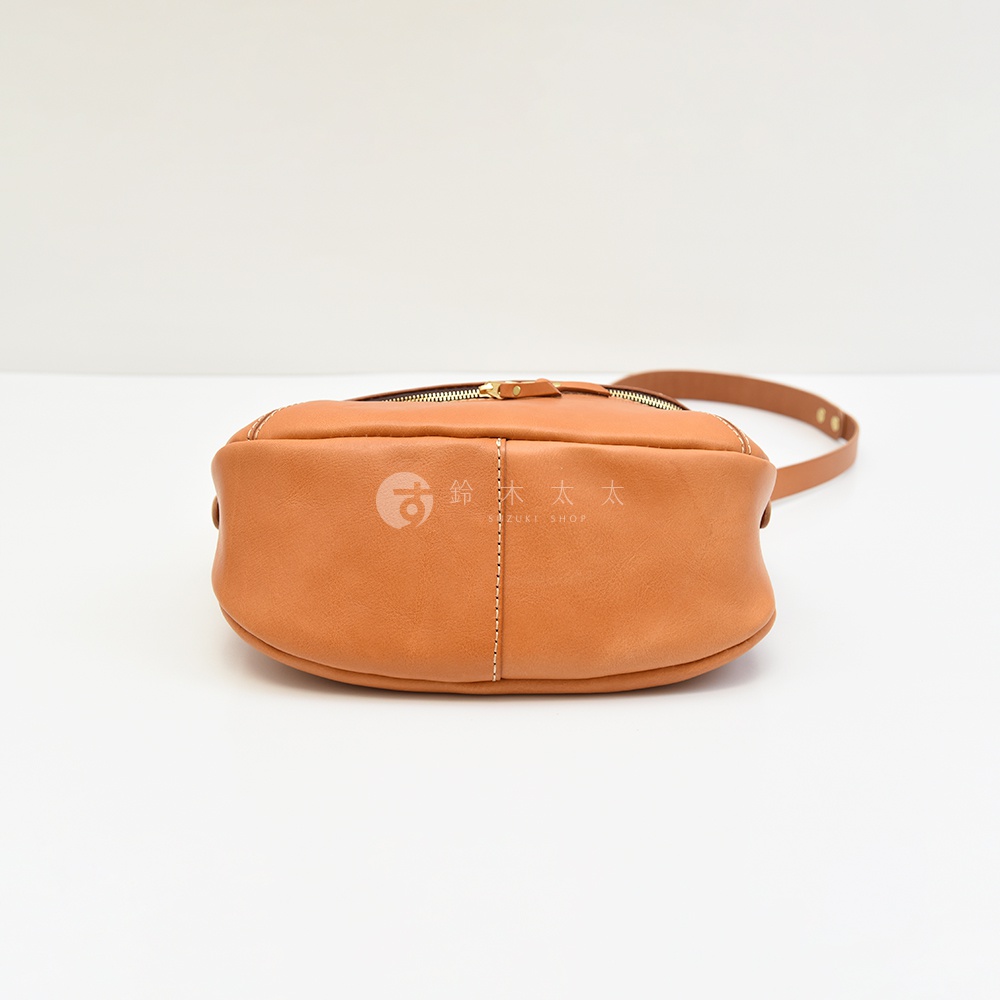 日本HERZ職人手作皮革大容量馬鞍包 CK-150，從底部視角展現焦糖棕色光滑皮革的光澤與縫線細節，上方可見品牌標誌。