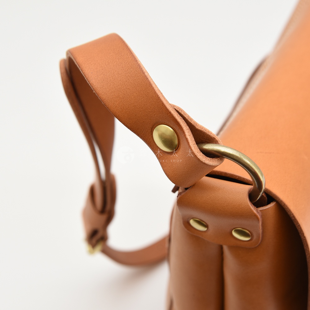 模式B： 簡潔的棕色皮革郵差包，特寫其精緻的皮質手提帶、金屬釦件及旋轉環細節。