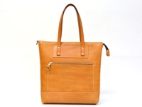 職人手作皮革威靈頓直式拉鍊托特包，呈現天然皮革的溫潤棕色調。包包設計簡潔，正面設有拉鍊口袋，並以精緻的縫線點綴。提把與包身結構穩固，散發質感。