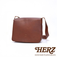 一個棕色的皮革斜背包，正面壓印有「Z」字樣，下方有「HERZ HAND MADE IN JAPAN Since1973」的品牌標誌。