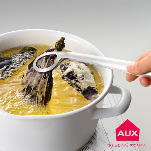 白色炸鍋中，熱油翻滾，一只手正用銀色金屬炸物夾夾起一塊炸好的茄子。夾子設計簡潔，有環狀開口。