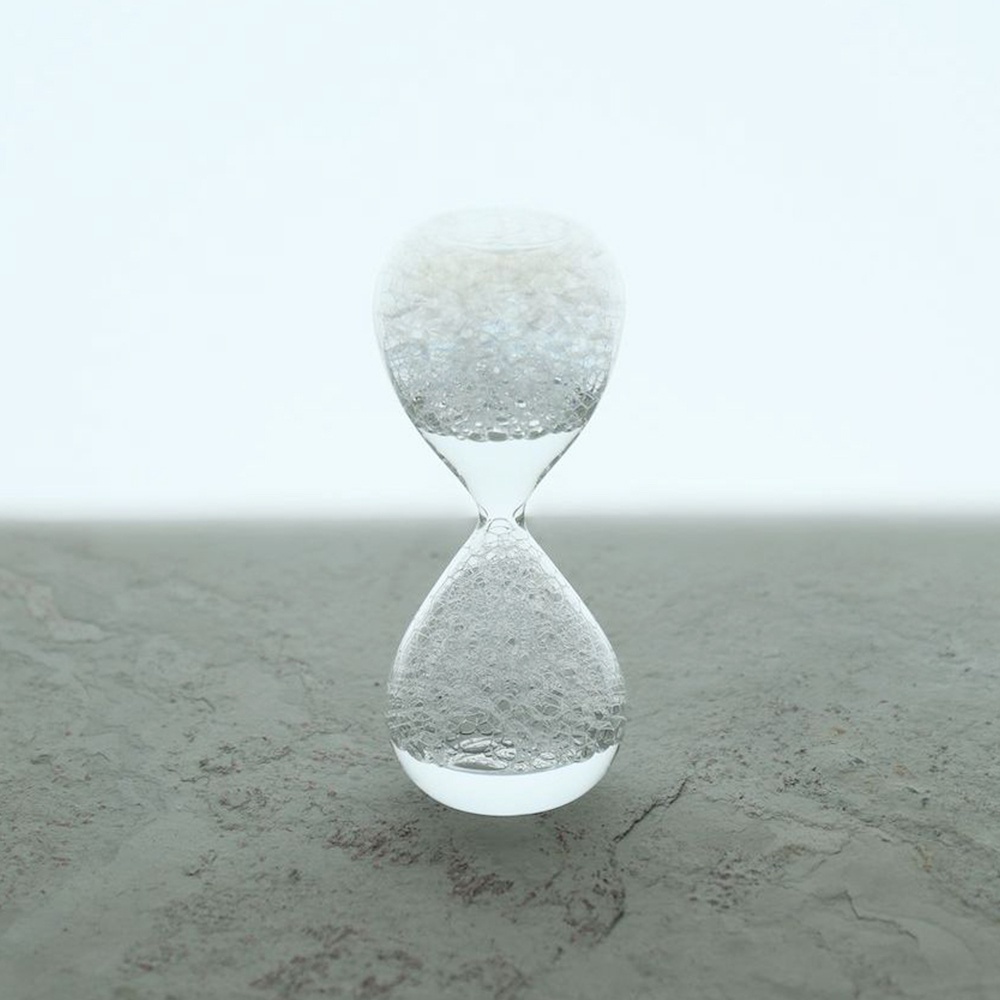 awaglass mini 泡時計/沙漏，透明玻璃製成，內部充滿細小氣泡，呈現獨特視覺效果，放置於灰色紋理表面上。