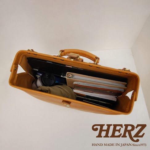 職人手作皮革軟式杜勒斯包，淺棕色皮革，包內裝有筆記本、文件夾、筆記型電腦和保溫杯。