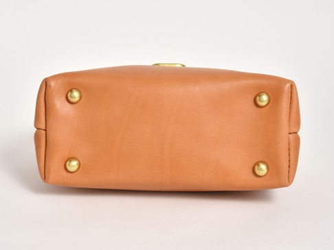 職人手作皮革兩用迷你口金單肩包 (CW-7) 的底部，呈現光滑的棕褐色皮革材質，設有四個黃銅色的金屬腳釘，用於保護包底。