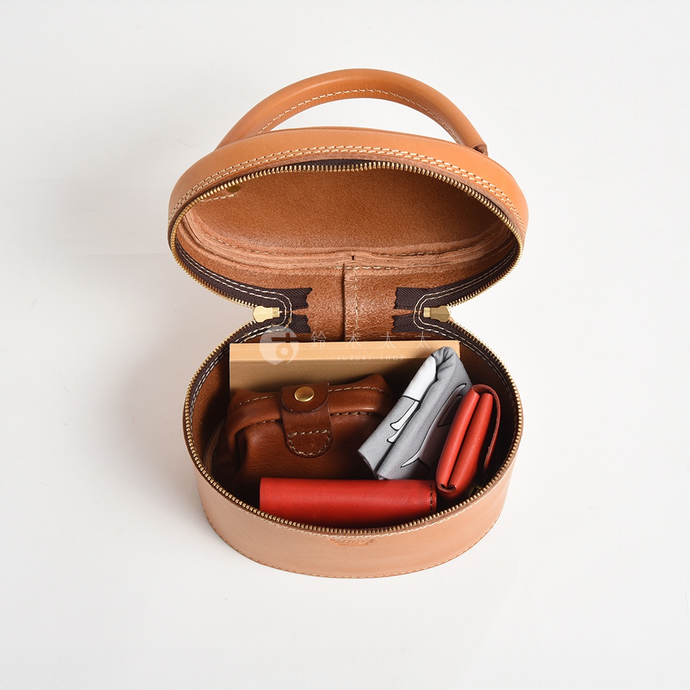職人手作皮革圓筒型化妝手提包，淺棕色皮革，拉鍊開合，內部裝有棕色皮革小包、紅色小物及灰色印花布料。