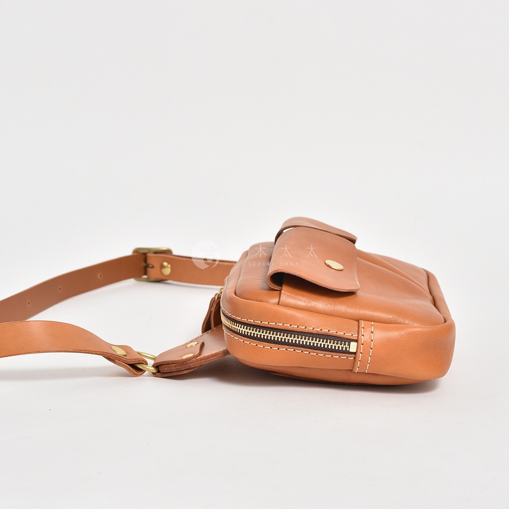 棕色皮革雙口袋斜背包，側面有拉鍊及按扣，搭配可調節的皮革揹帶和黃銅金屬扣環。