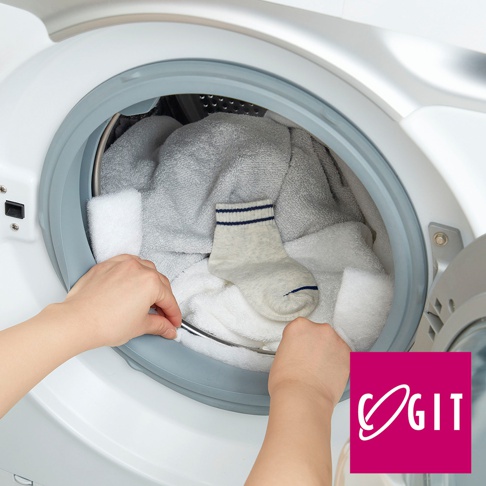 白色滾筒洗衣機門縫，一隻手正將白色海綿條塞入門縫，另一隻手拿著一隻淺灰色條紋童襪，洗衣機內有白色及灰色毛巾。